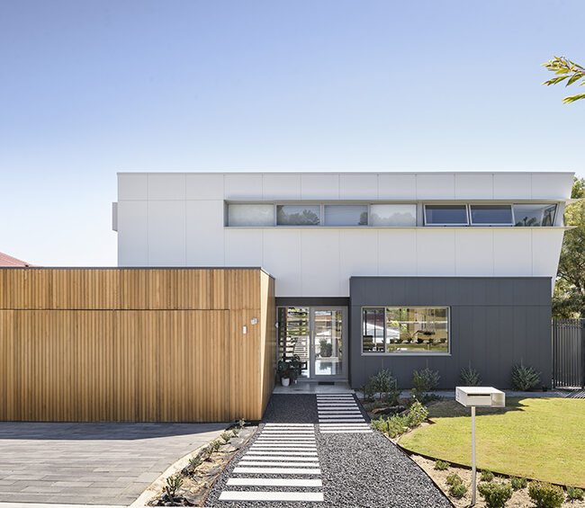 A modern home featuring a wooden front door and a paved driveway leading up to the entrance.