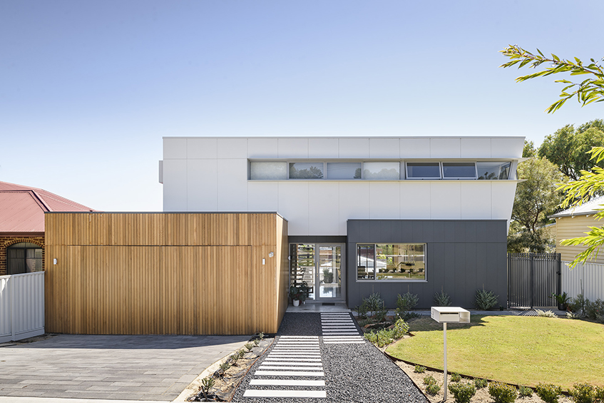 A modern home featuring a wooden front door and a paved driveway leading up to the entrance.