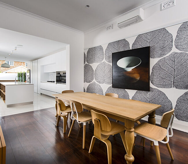 A dining room featuring a wooden table surrounded by four chairs, with warm lighting and decorative elements.